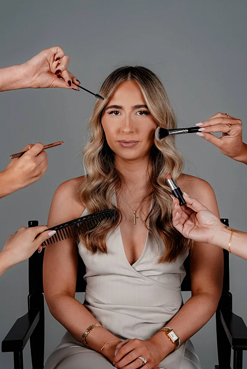 Tiana Loprete surrounded by hands holding makeup brushes, a lipstick and a comb